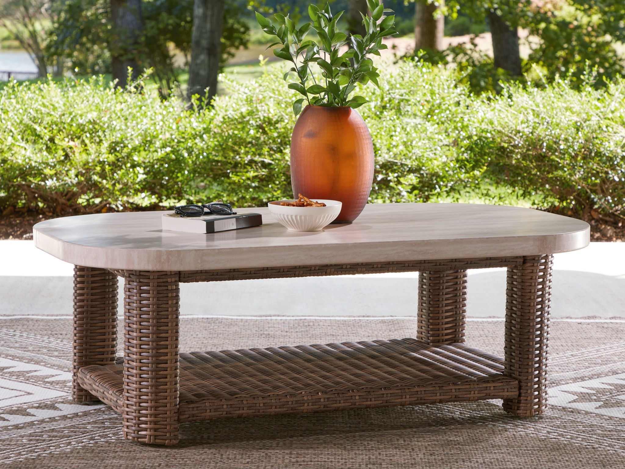 Rectangular cocktail table with light beige top and woven wicker frame, open storage shelf