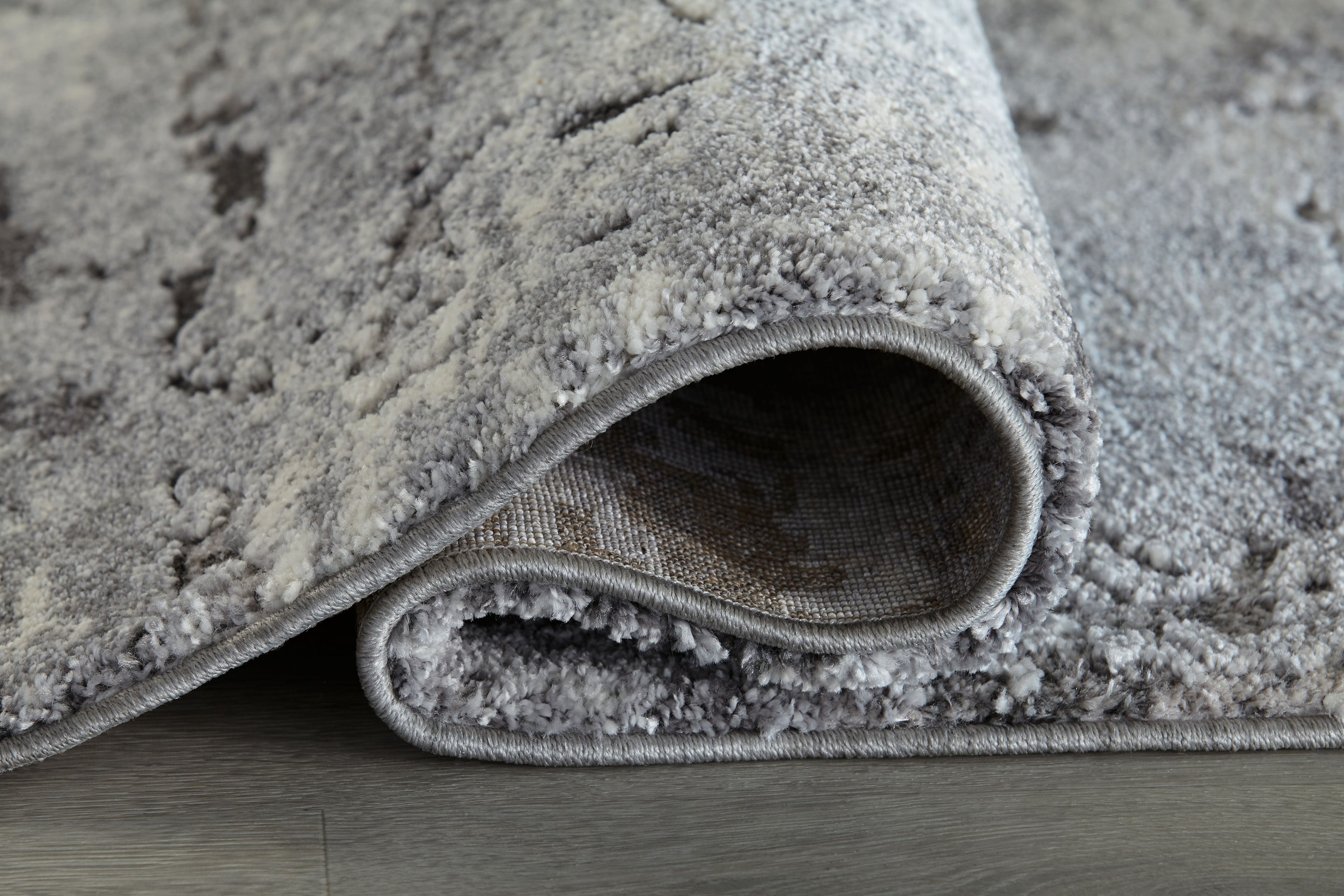 Dark gray area rug close-up of braided edge and plush pile underside