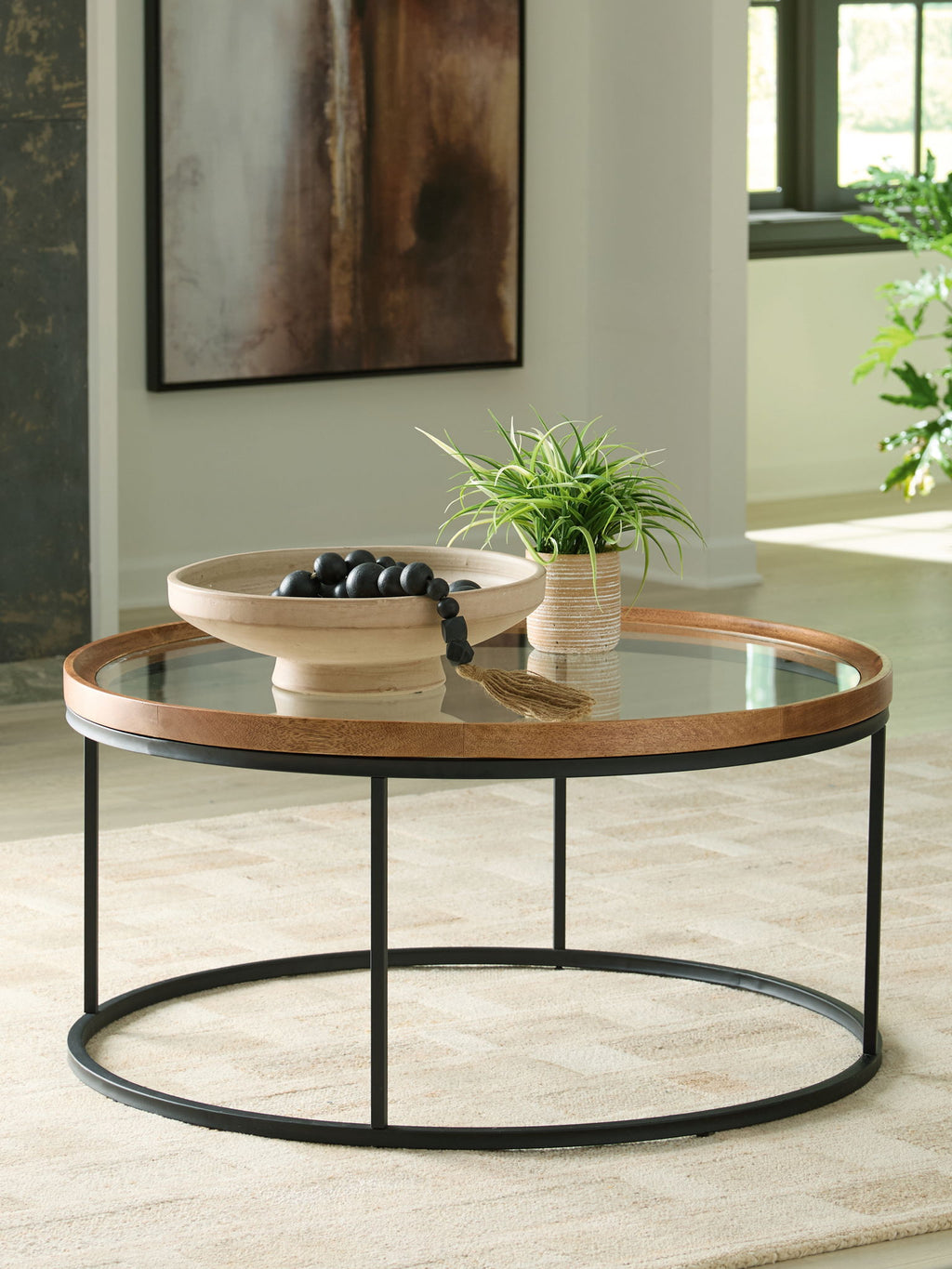 Round side table with clear glass top and light brown wood rim, black frame, lower shelf