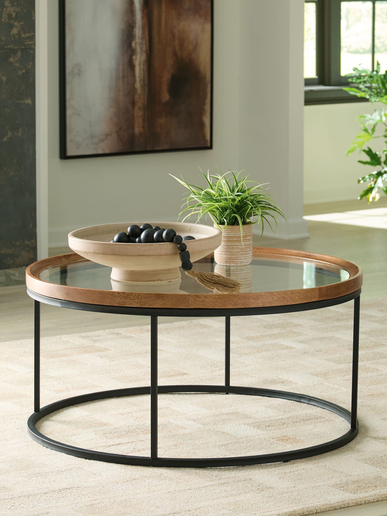 Round side table with clear glass top and light brown wood rim, black frame, lower shelf
