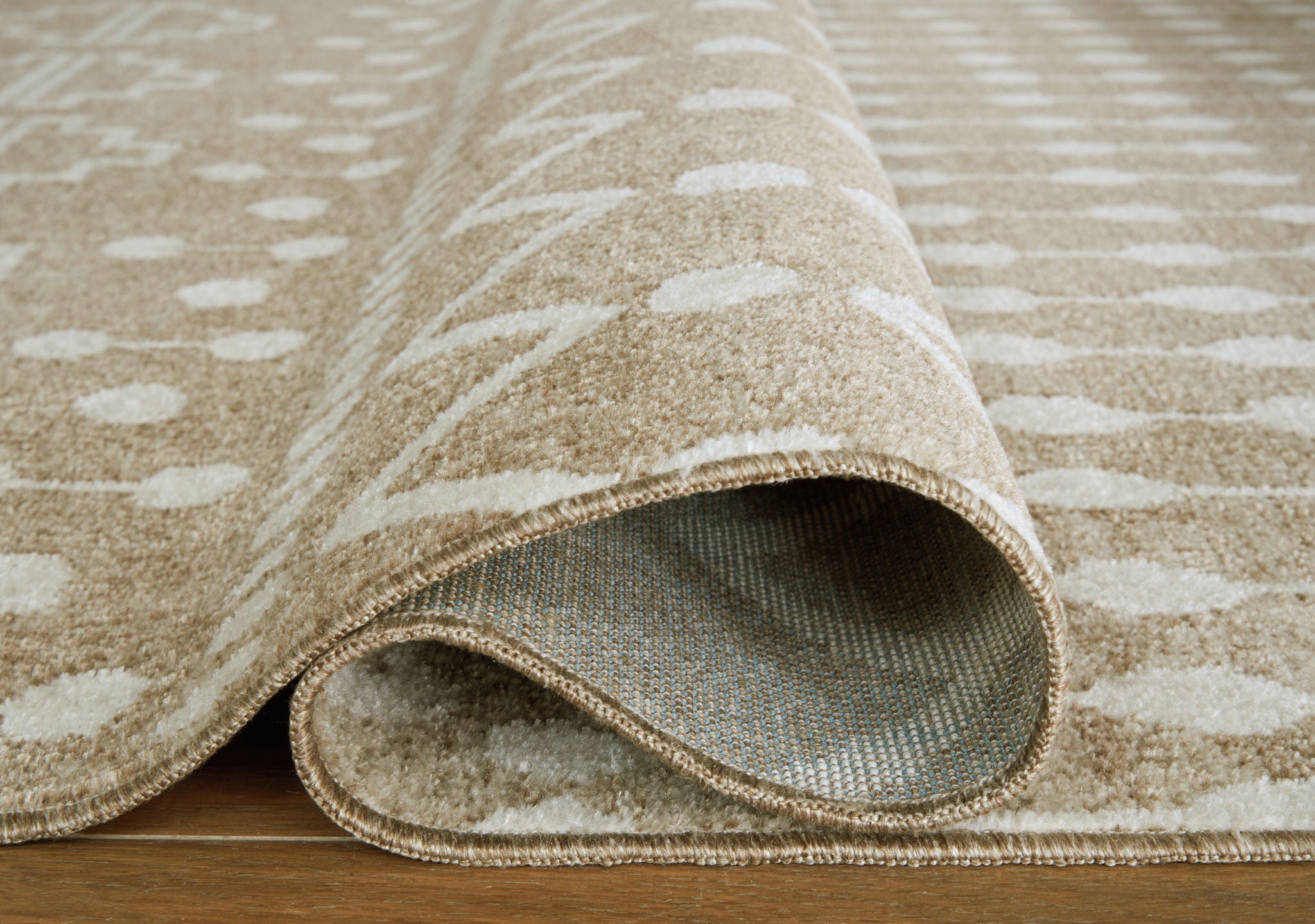Tan geometric rug roll edge with low-profile bound hem and visible underside backing