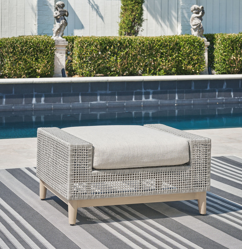 Gray outdoor ottoman with woven sides and padded cushion on light wood legs