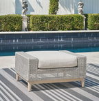 Gray outdoor ottoman with woven sides and padded cushion on light wood legs