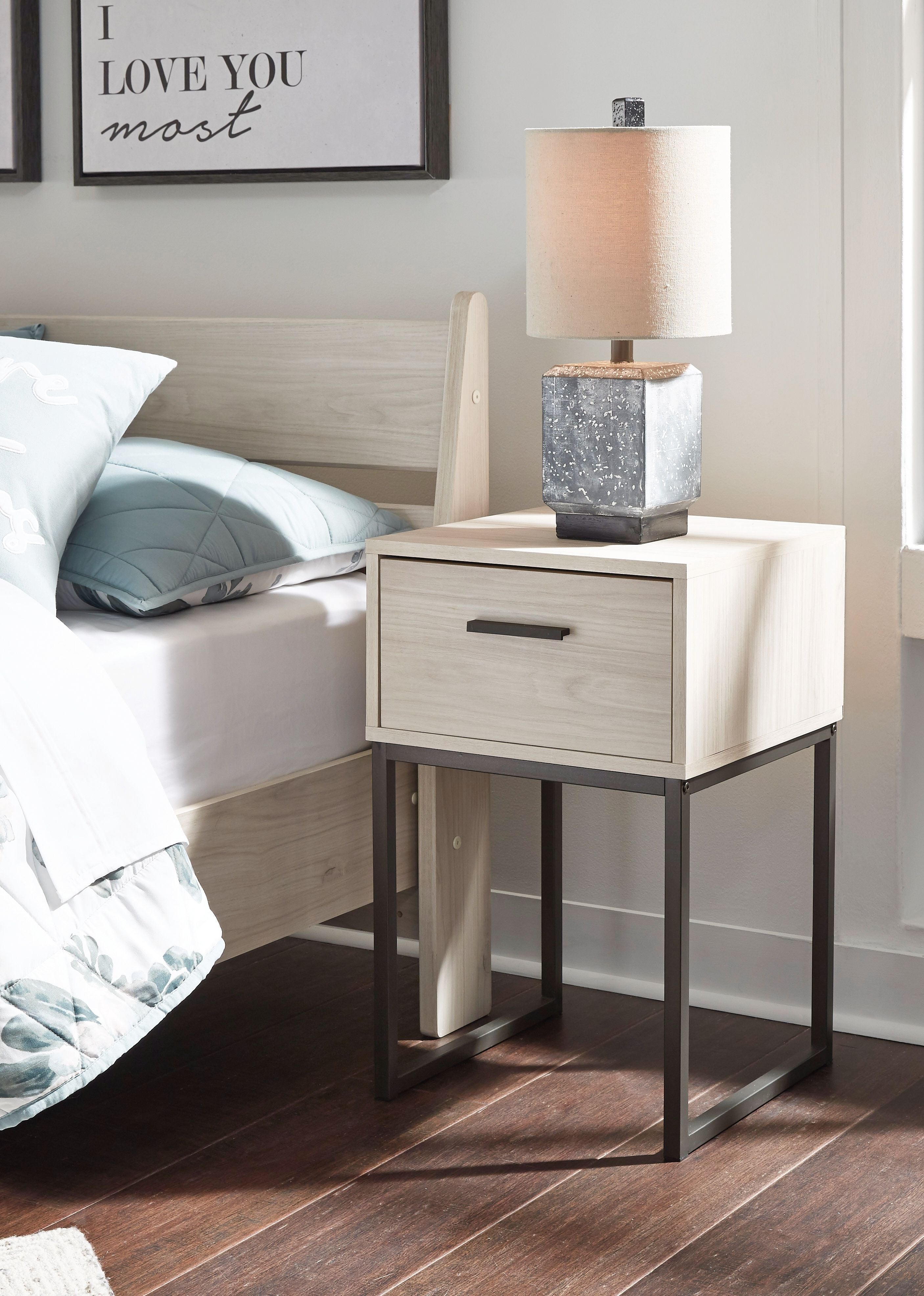 Light natural one-drawer nightstand beside bed with dark metal legs