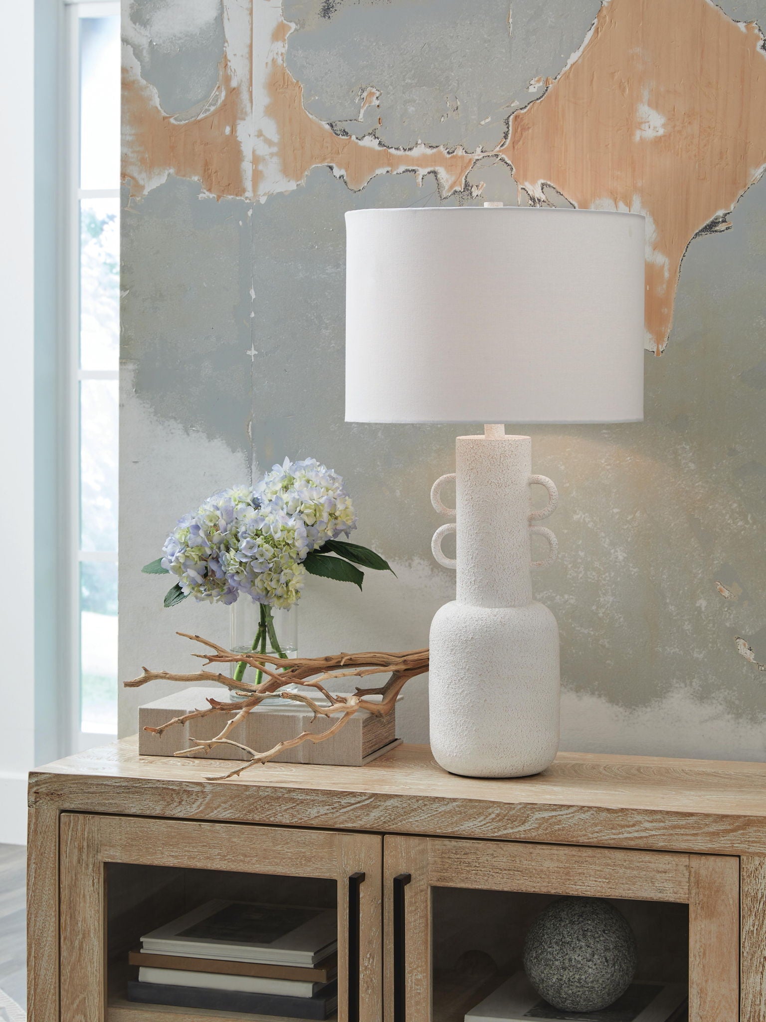 Distressed white metal table lamp with fabric drum shade over textured pedestal