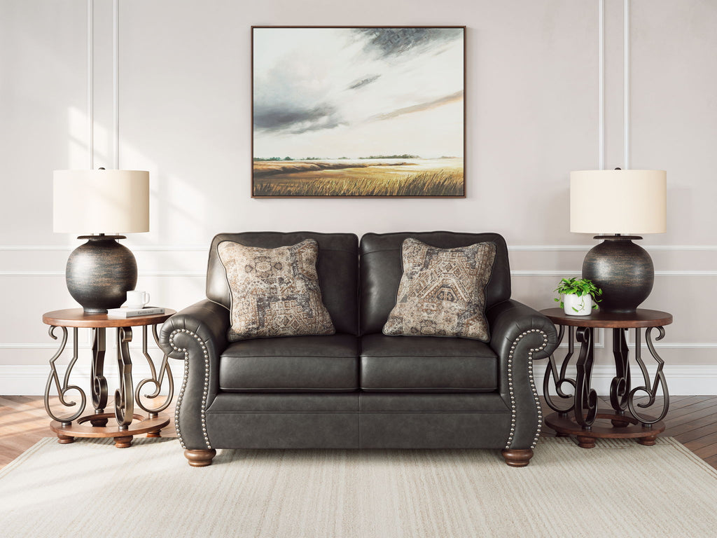 Dark gray loveseat with two patterned throw pillows and studded arm details