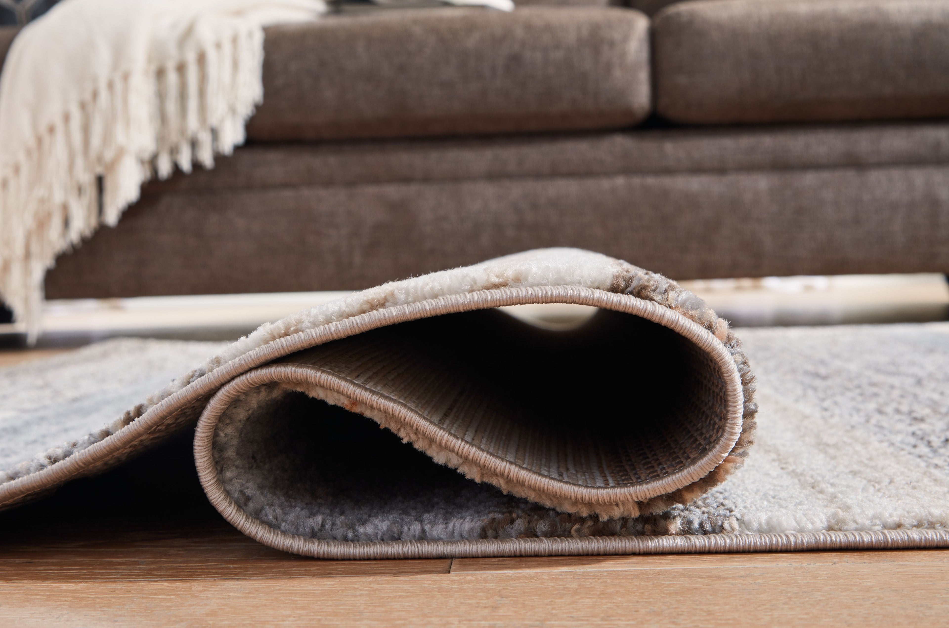 Gray rug corner with visible rounded edge binding and short pile