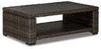 Brown wicker rectangular cocktail table with black glass top and lower shelf