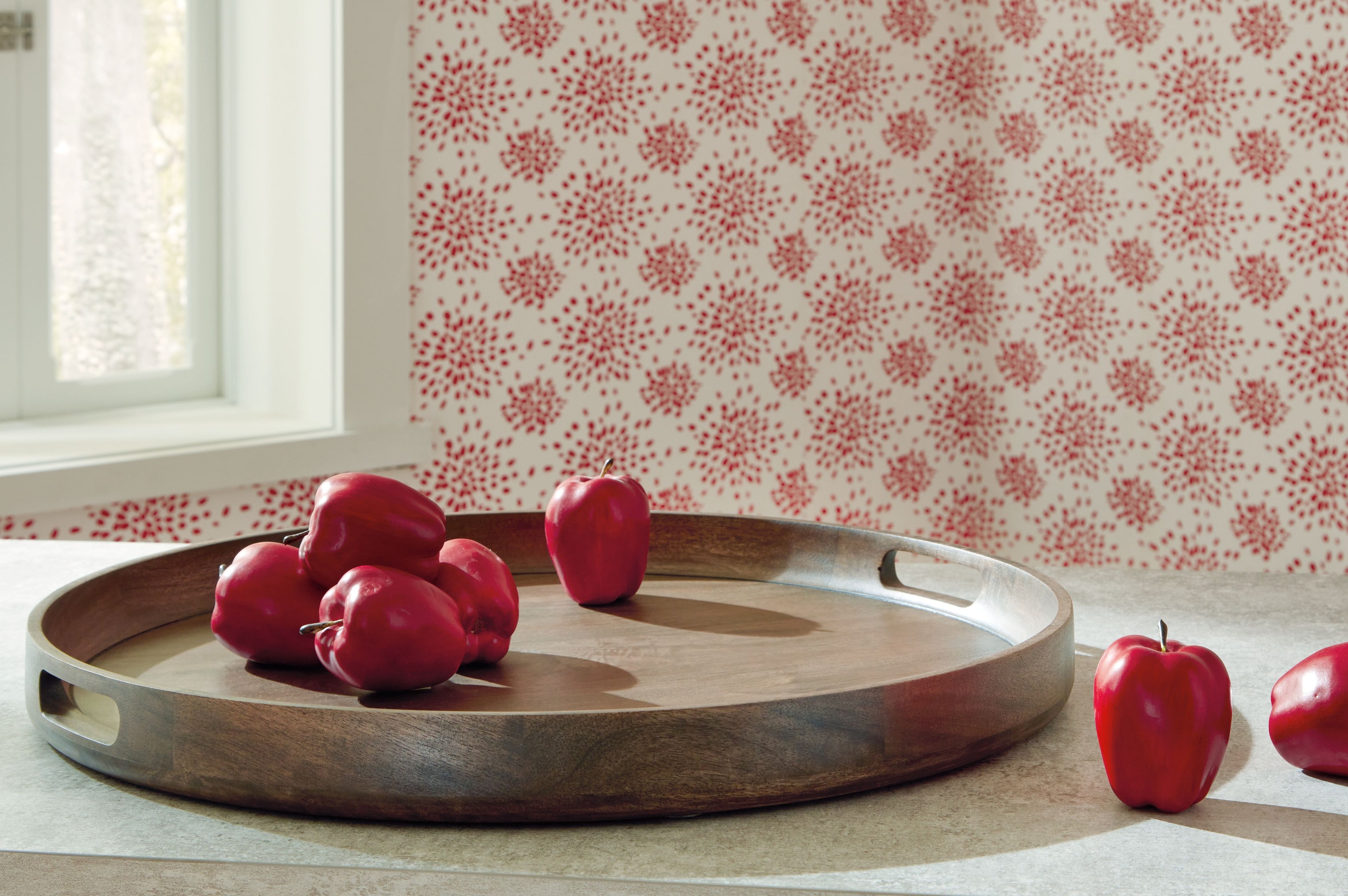 Gray-brown wooden round tray with handle cutouts, topped with red peppers