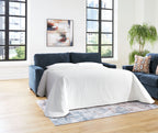 Sofa sleeper opened into a bed with dark blue upholstery, white cover, and side pillows.