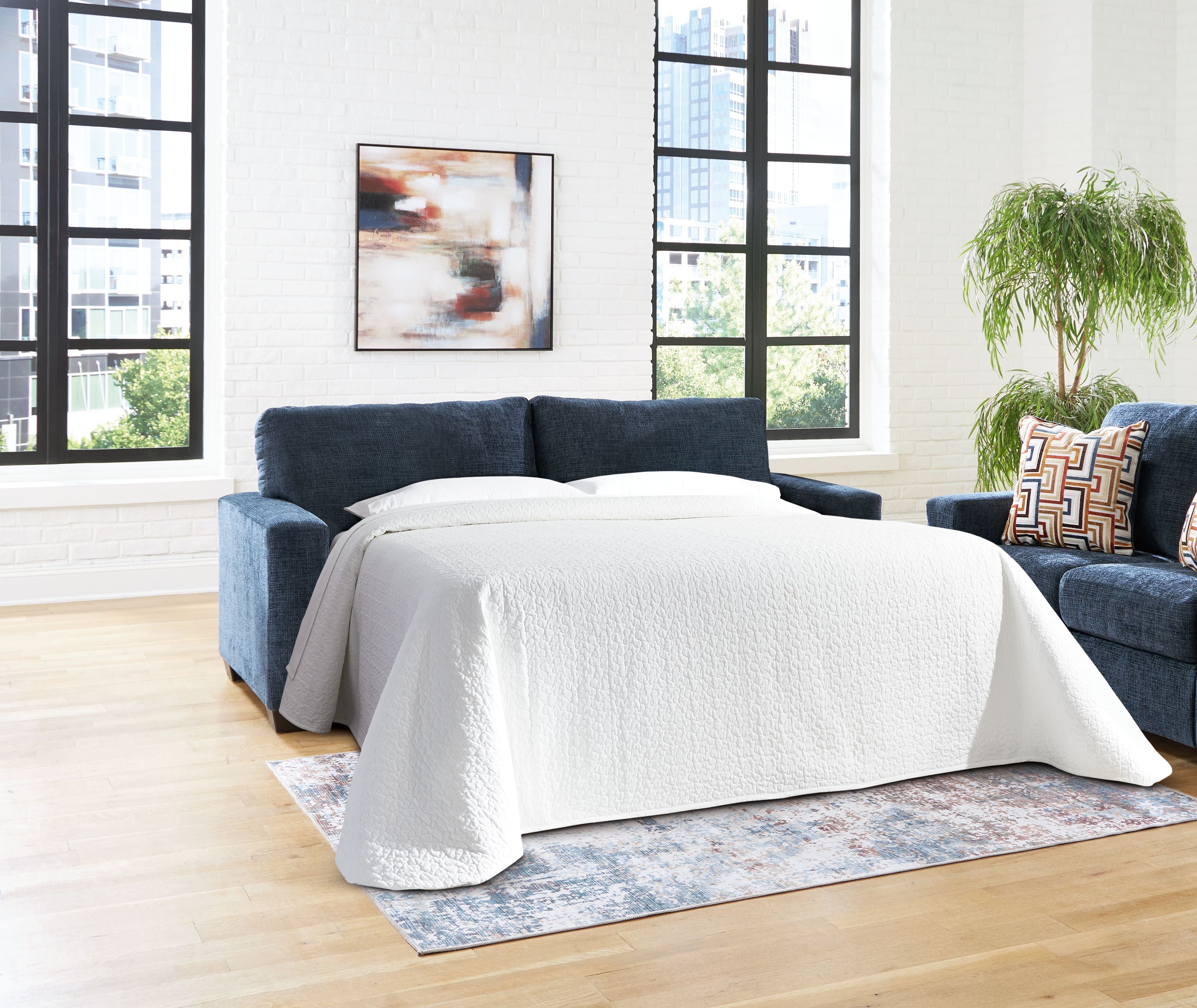 Sofa sleeper opened into a bed with dark blue upholstery, white cover, and side pillows.