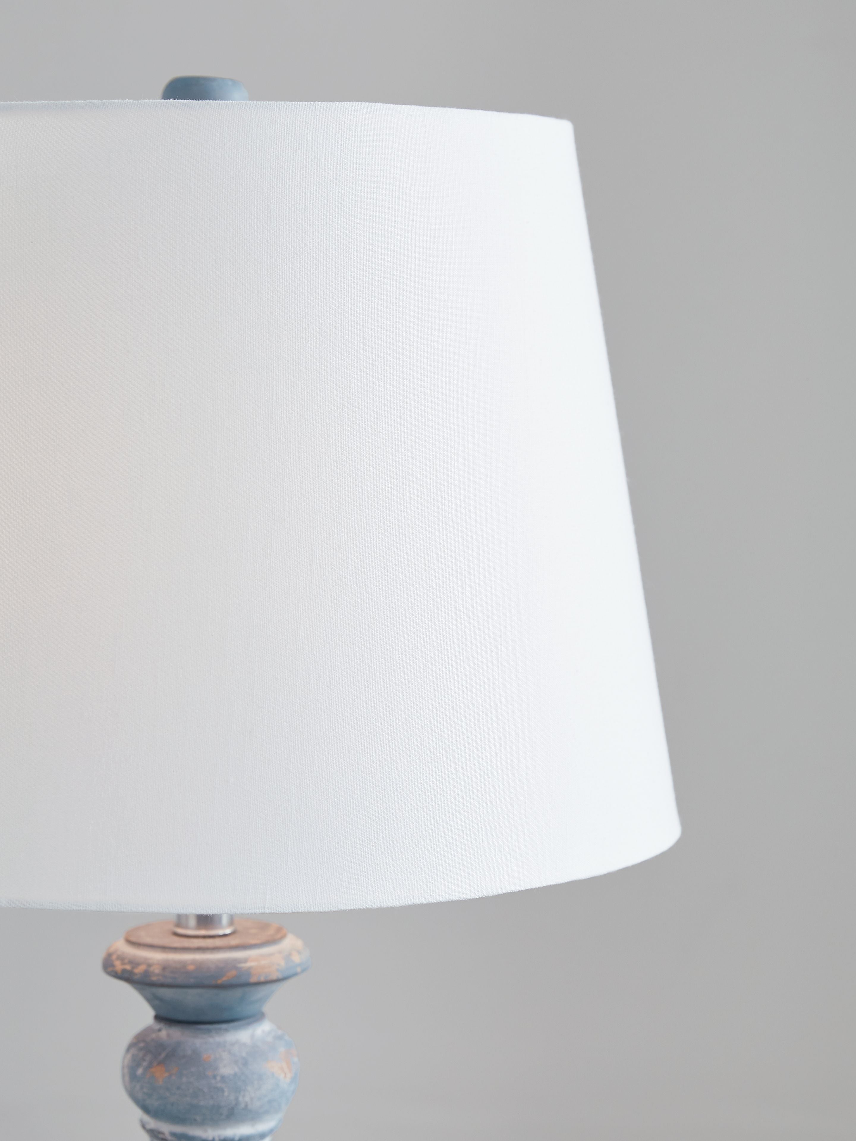 Antique blue table lamp with white fabric shade, close-up of base top