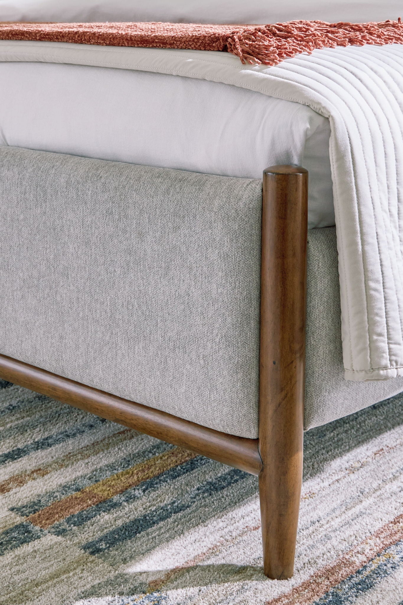 Upholstered bed frame with grey upholstered base and dark brown wooden legs, corner view