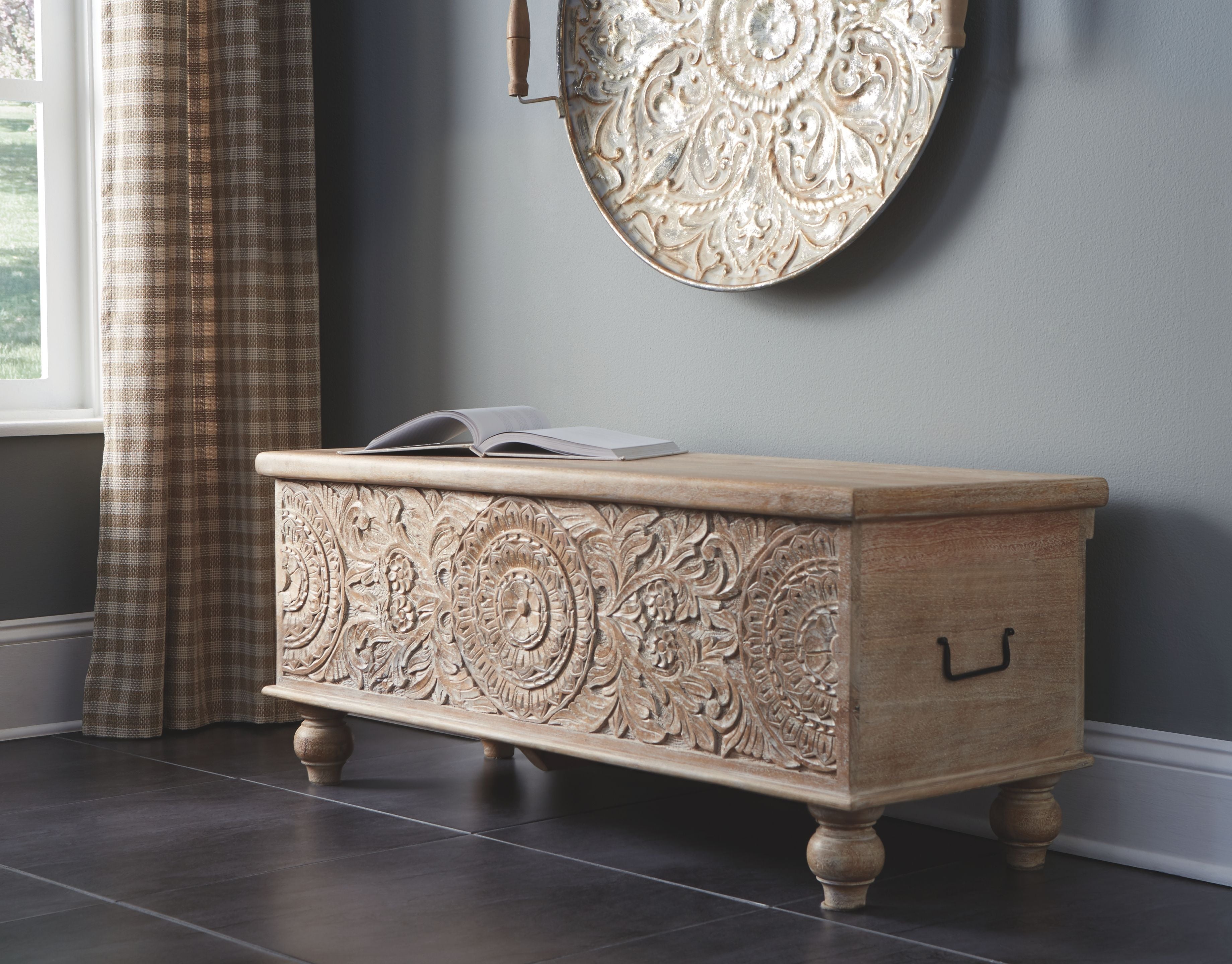 Beige storage bench with ornate carved front, turned legs, and lift-up lid