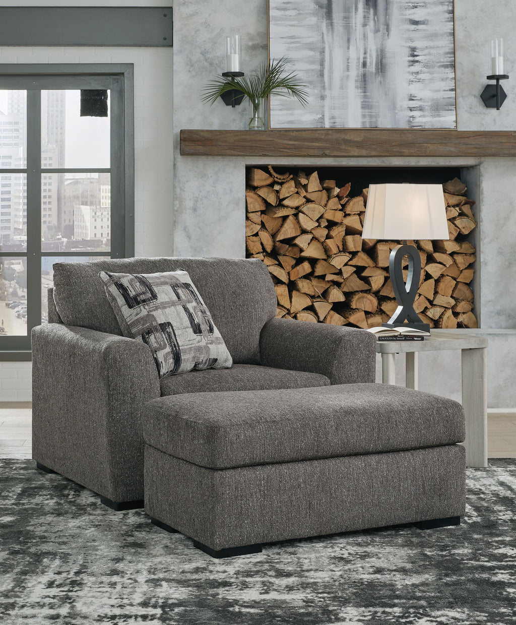 Pewter upholstered chair and a half with patterned pillows, ottoman-style base