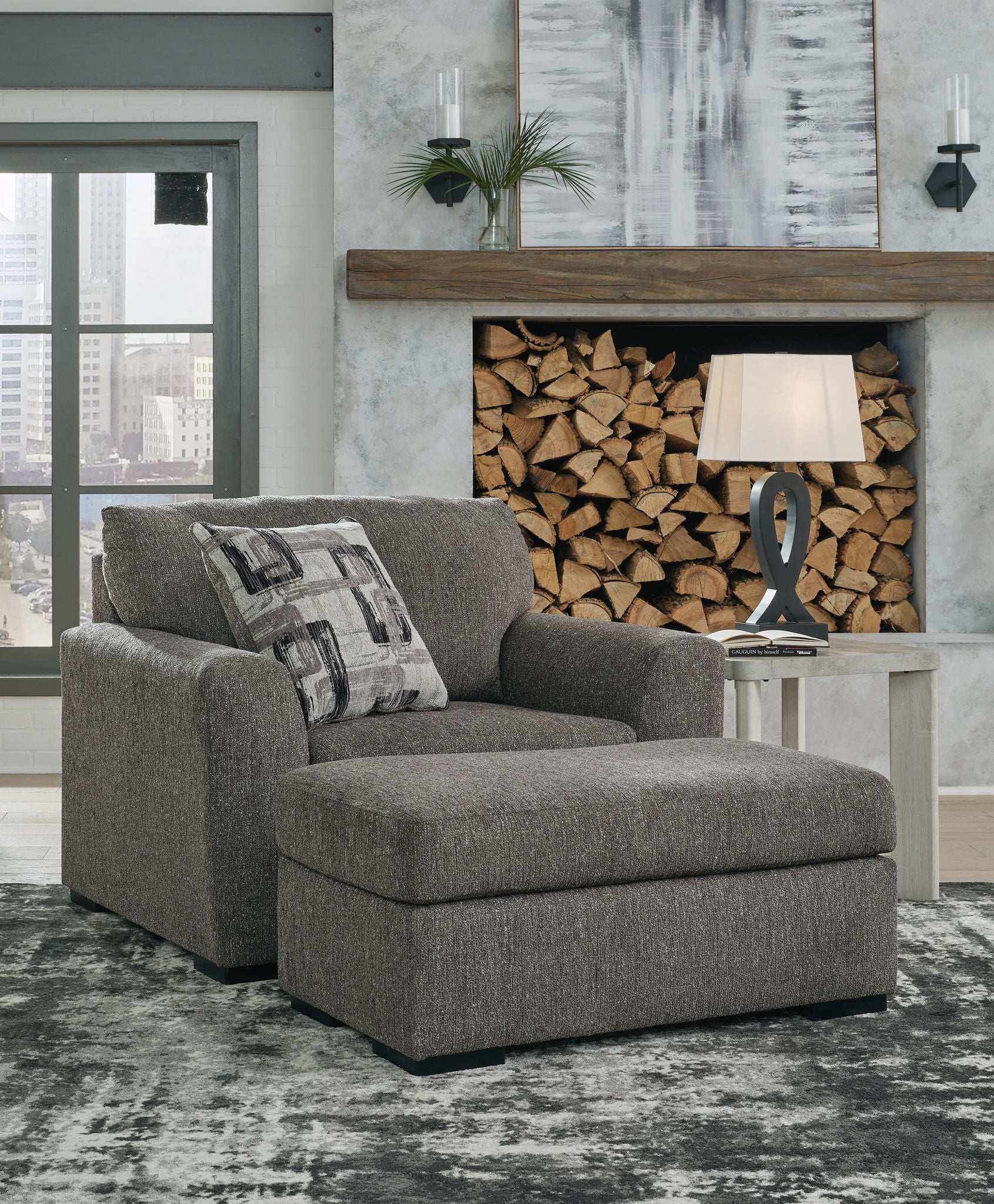 Pewter upholstered chair and a half with patterned pillows, ottoman-style base