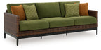 Wicker lounge sofa with green cushions, patterned green pillows, and brown accent cushions