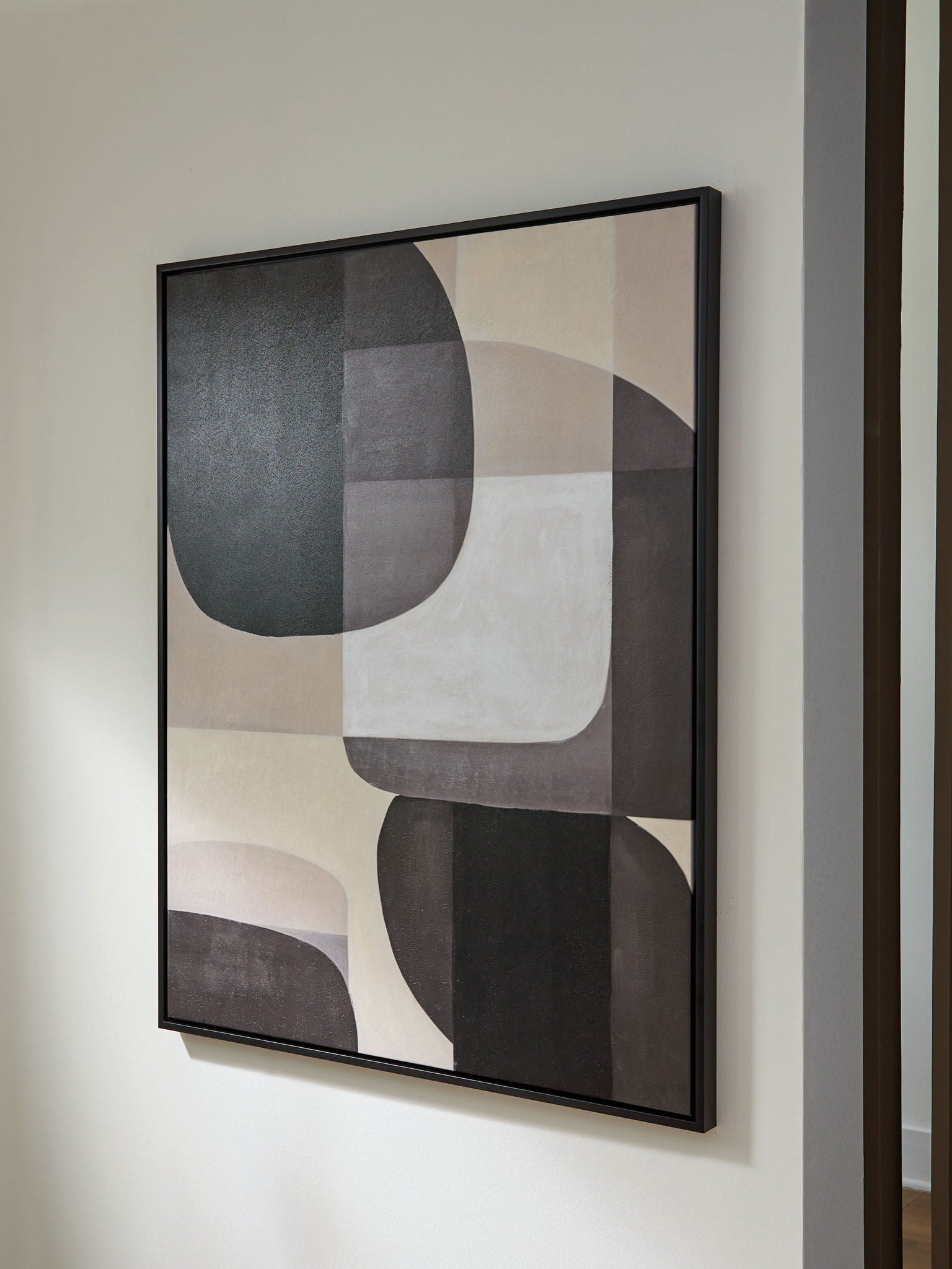 Framed abstract wall art on wall with black and white overlapping oval and rectangle forms.