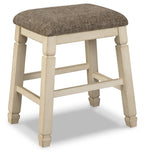 Upholstered stool with textured neutral fabric seat and light wood turned legs, footrest