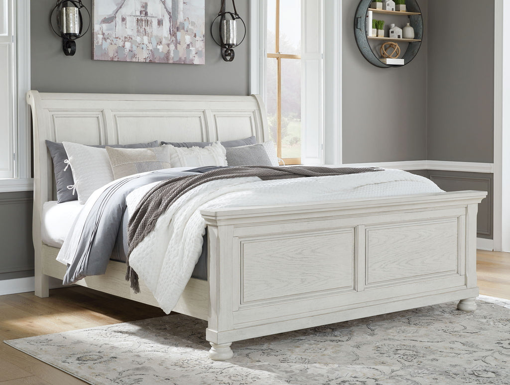 White sleigh bed with paneled headboard and footboard, shown with pillows and blanket.