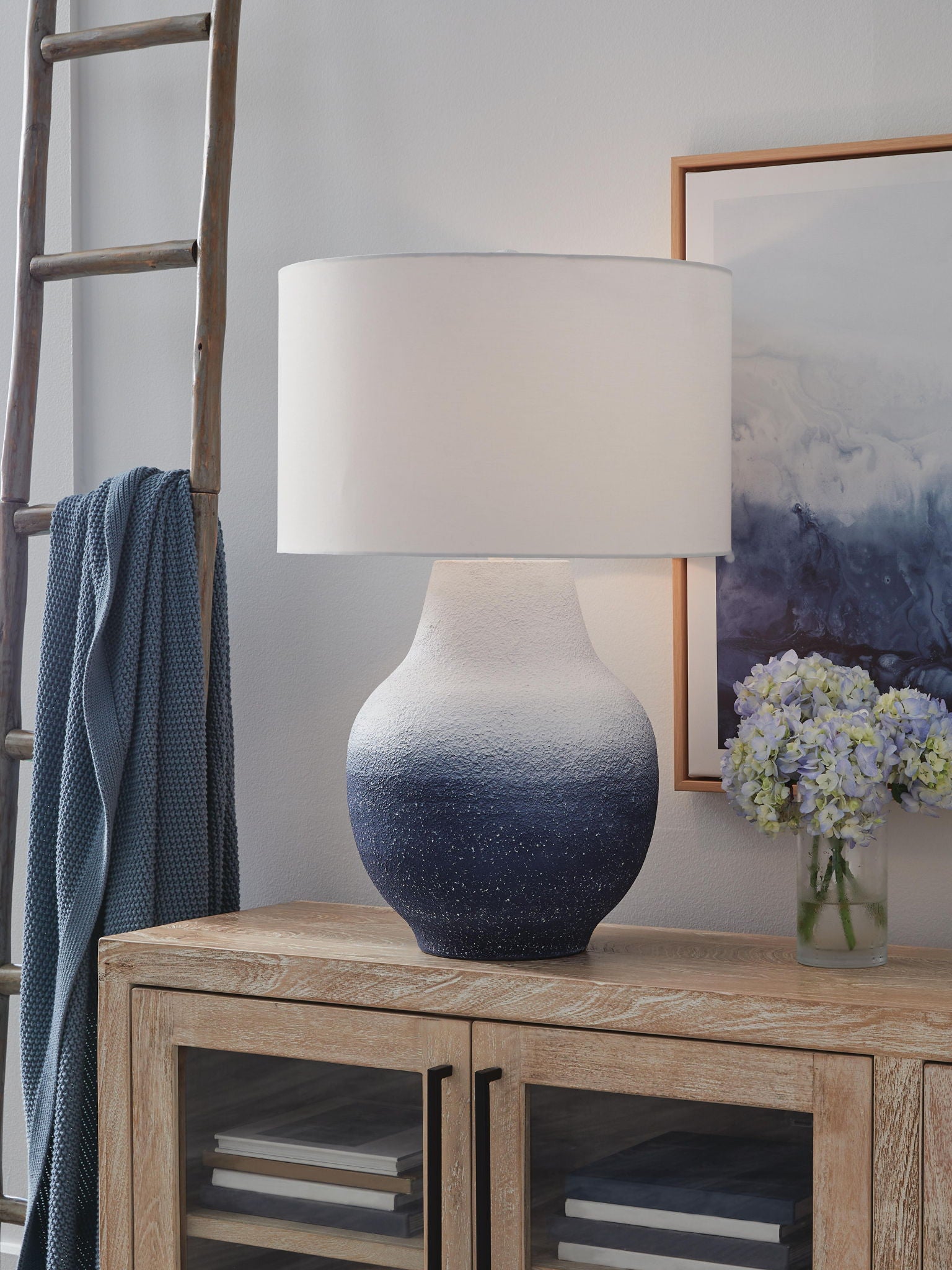Metal table lamp with white drum shade and speckled navy-to-white base on wood table