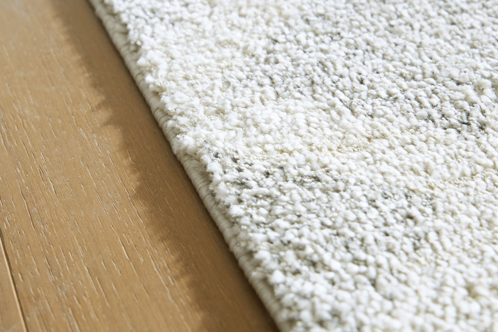 Gray rug edge with textured loop pile and backing fabric visible