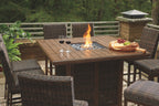 Outdoor fire pit table set with lit flame at center and woven barstools