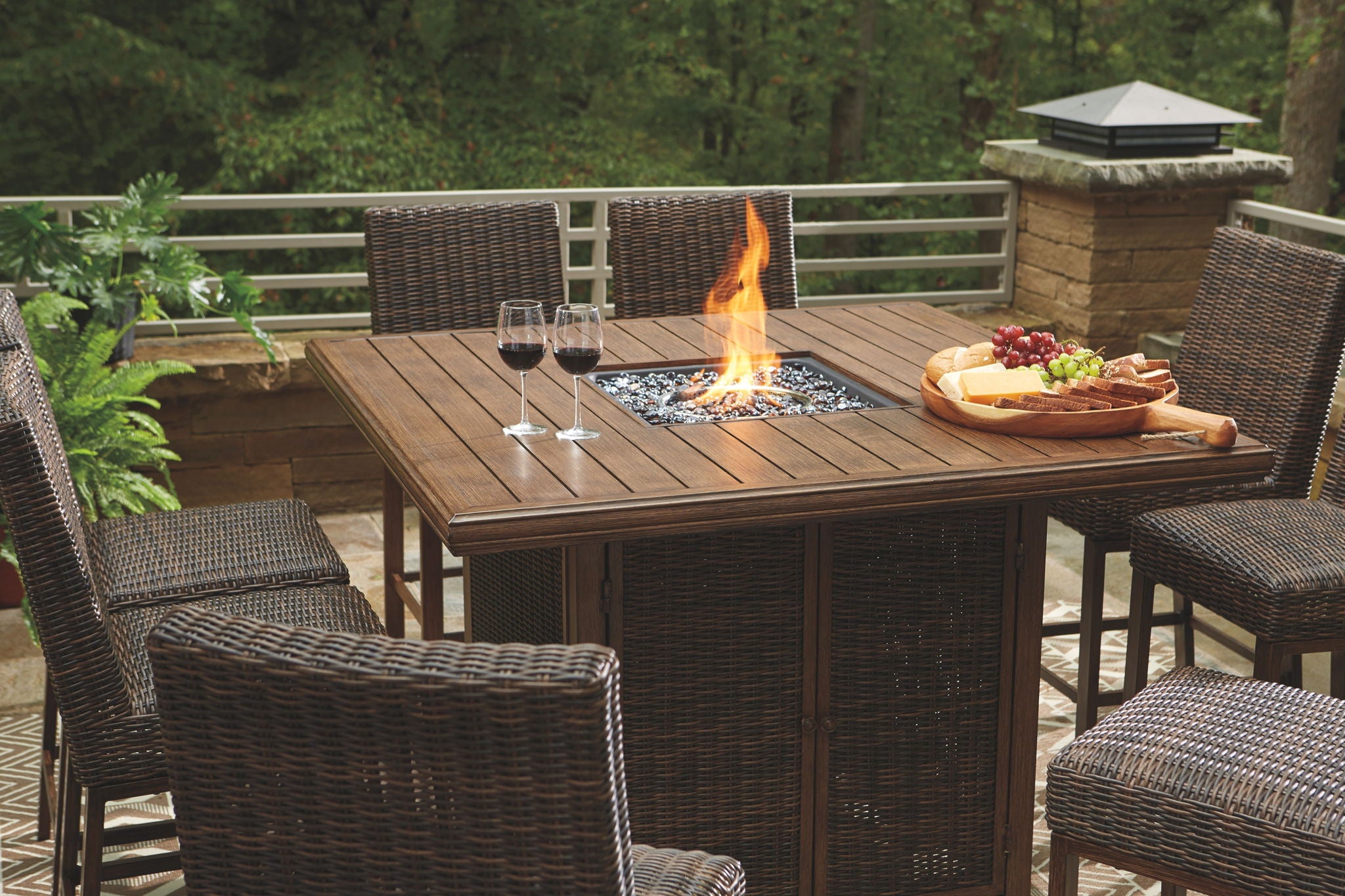 Outdoor fire pit table set with lit flame at center and woven barstools