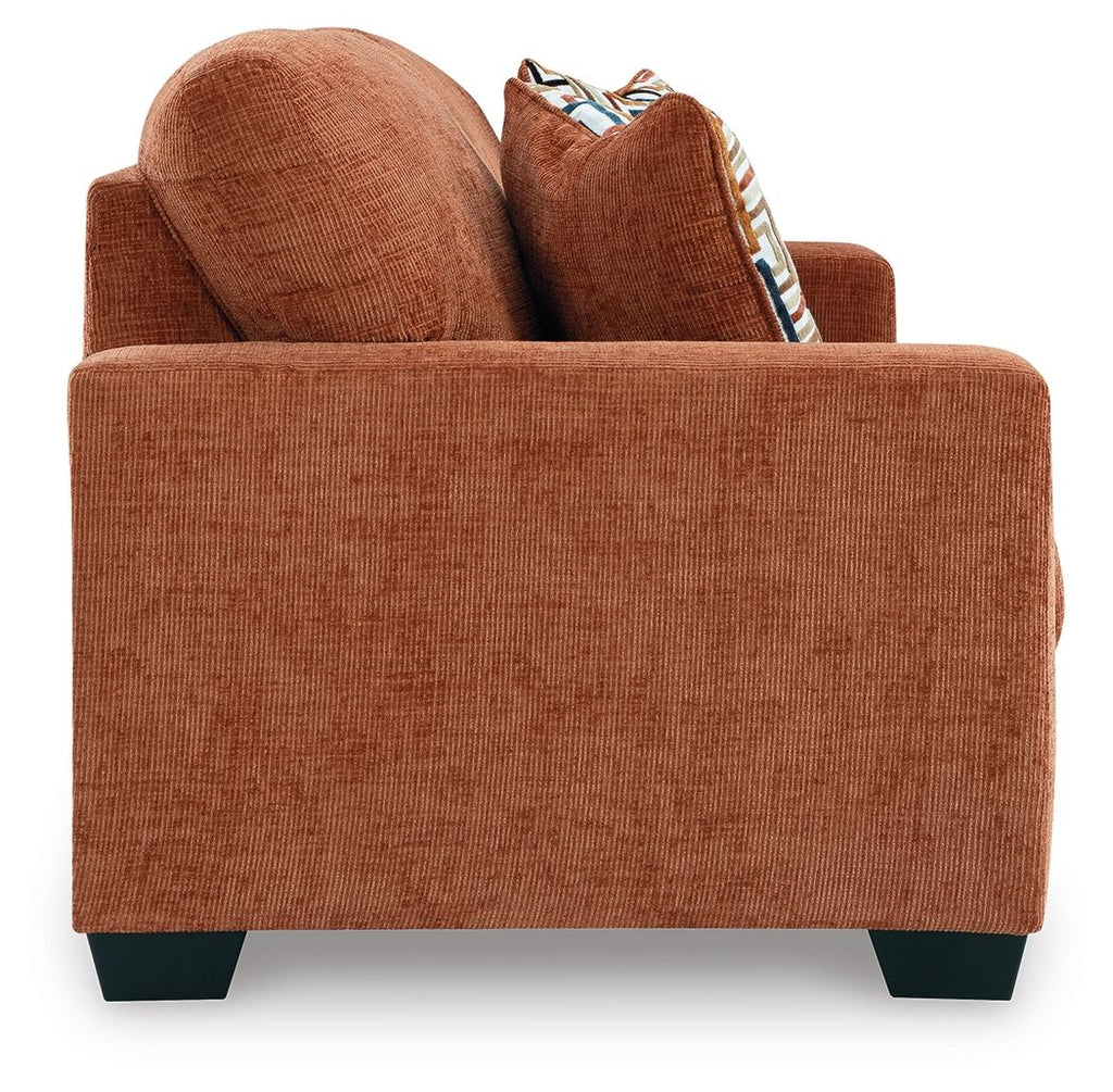 Rust orange upholstered sofa with textured fabric and two patterned throw pillows.