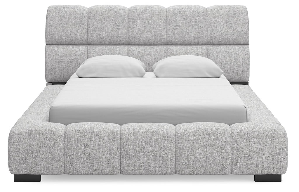 Gray upholstered bed with tall padded headboard and blocky tufted frame, front view