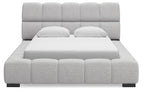 Gray upholstered bed with tall padded headboard and blocky tufted frame, front view