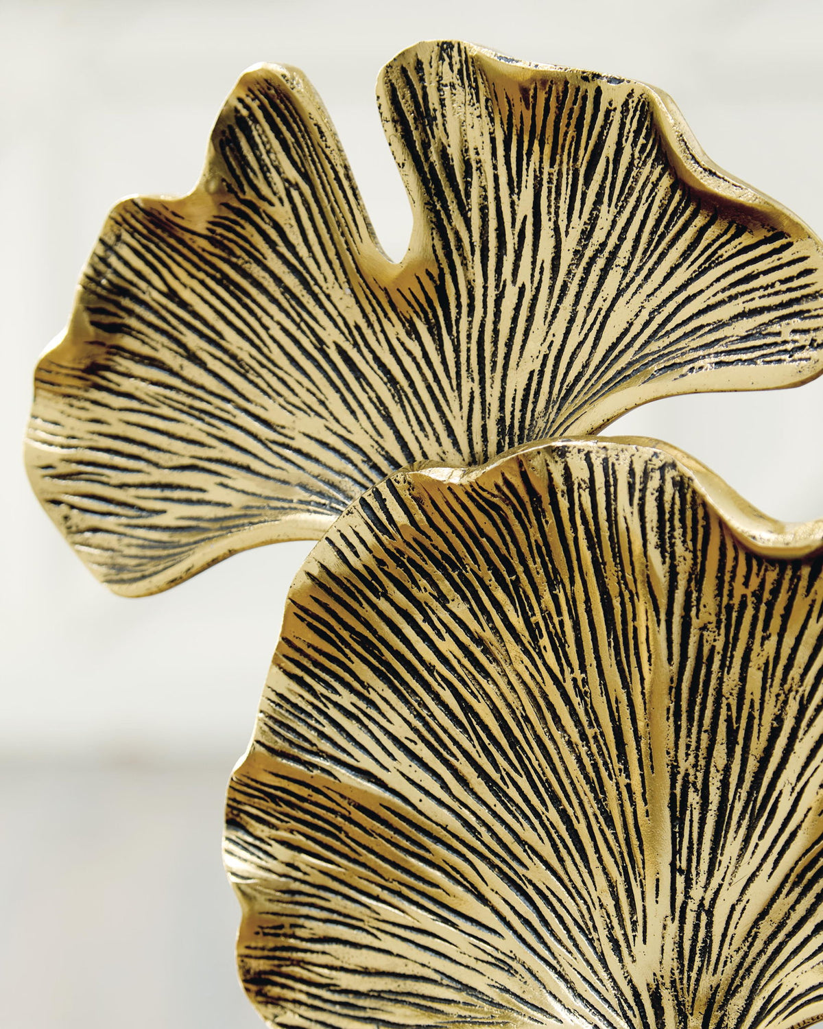 Close-up gold-finish abstract ginkgo leaves sculpture with dark base