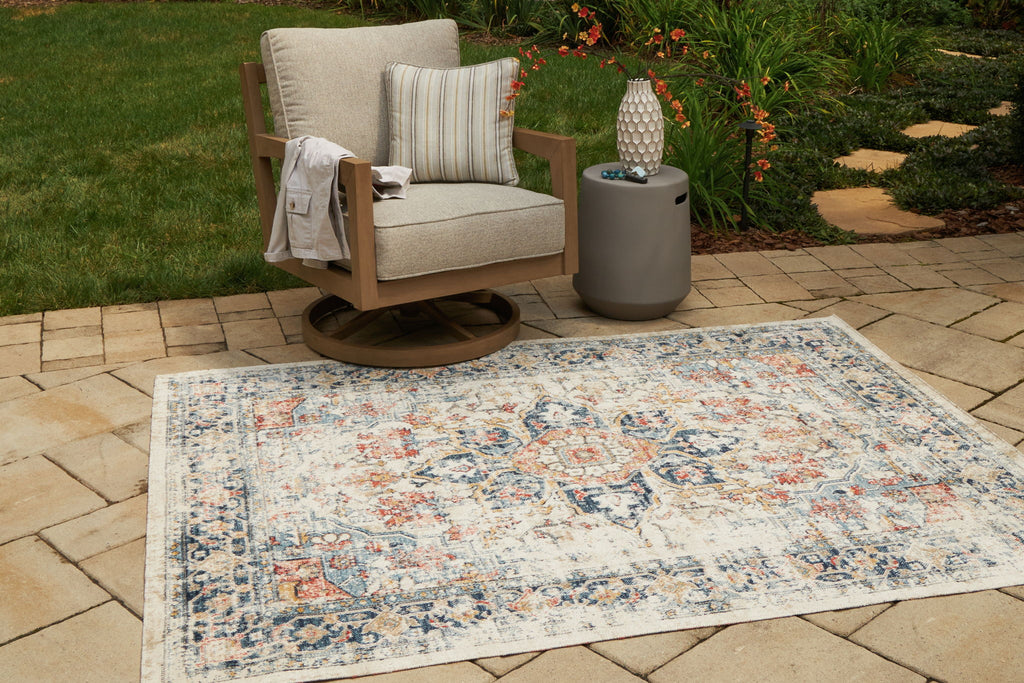 Multi-pattern area rug laid outdoors, rectangular cream base with blue and orange motifs
