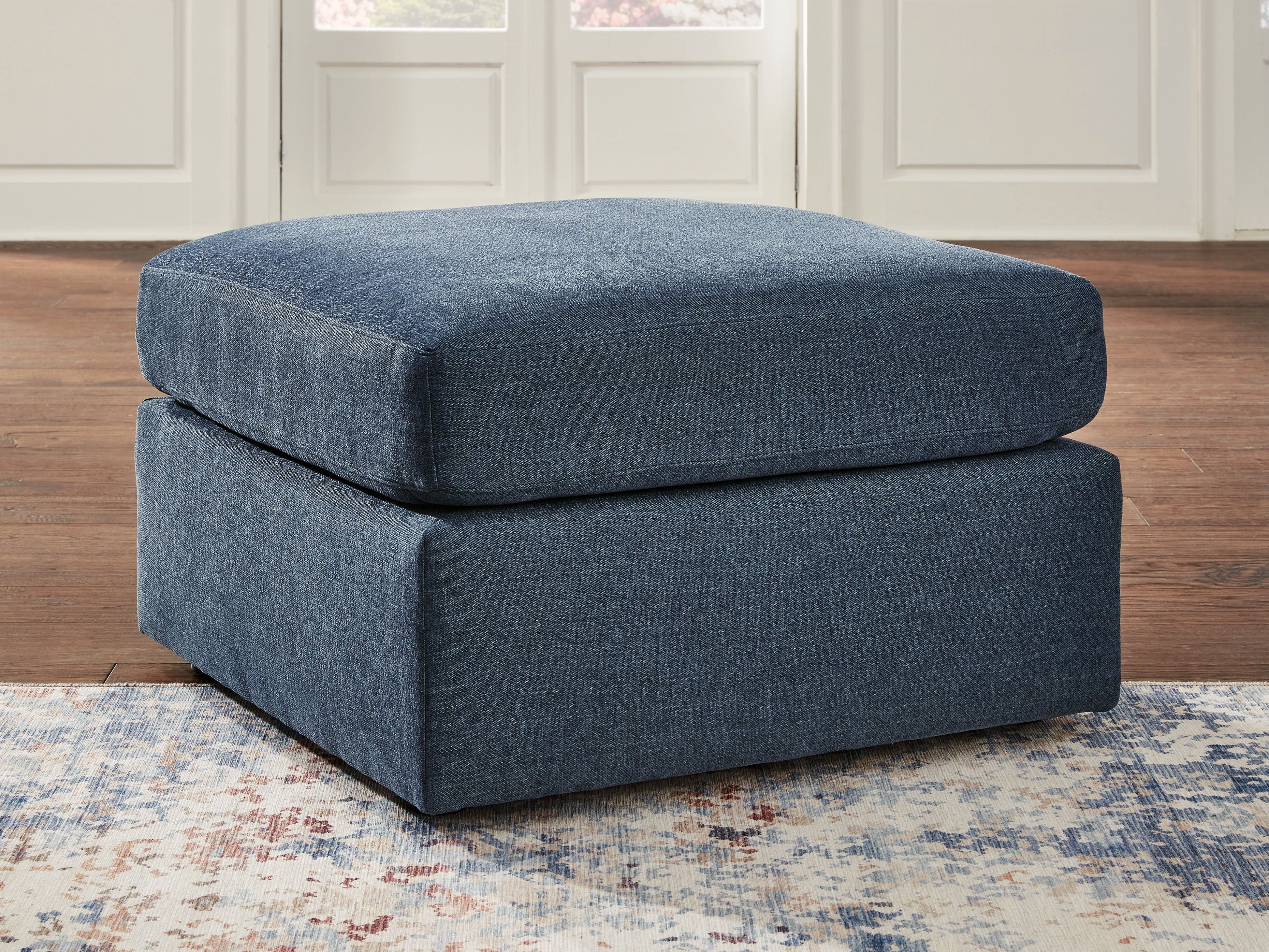 Ink blue fabric ottoman with thick seat cushion and low dark legs, front corner view