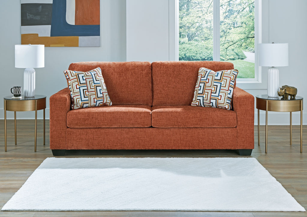 Rust-colored sofa with two patterned throw pillows and rolled arms