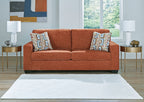 Rust-colored sofa with two patterned throw pillows and rolled arms