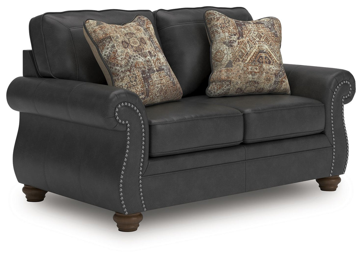 Dark gray loveseat with nailhead trim and two patterned throw pillows