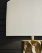White drum shade and gold metal neck of faceted table lamp