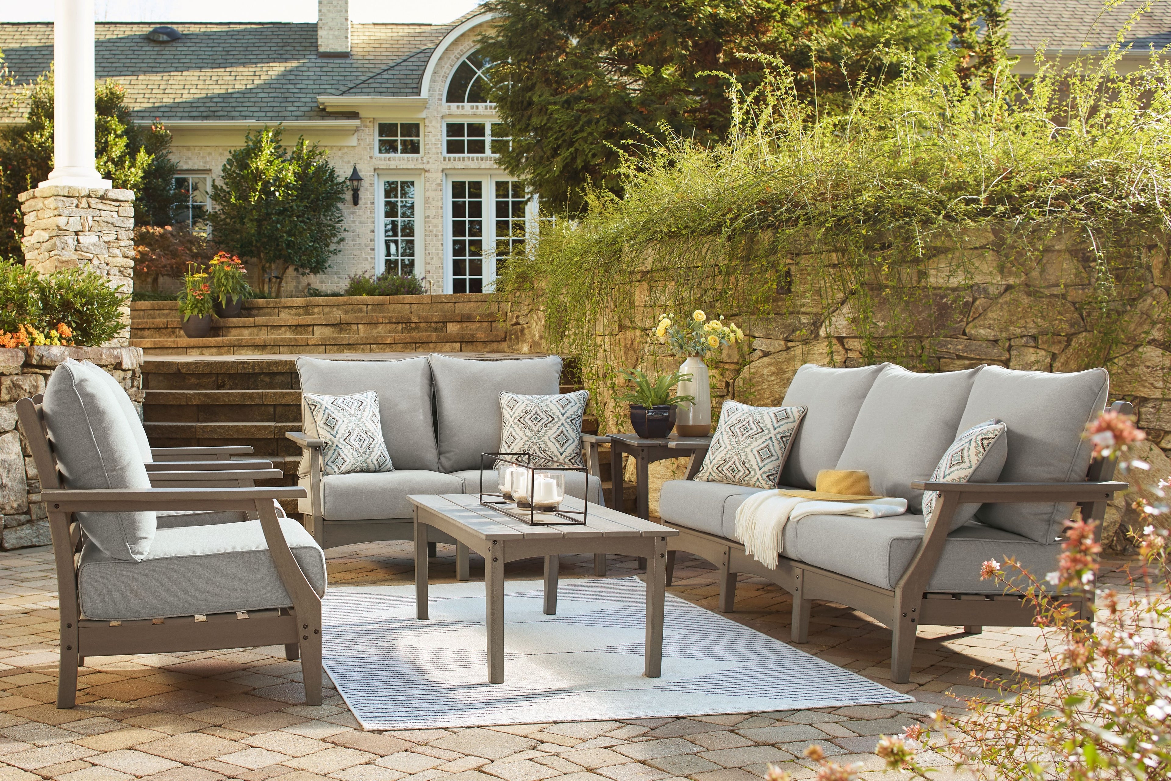 Gray outdoor lounge set with sofa, chairs, and coffee table; patterned accent pillows