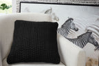 Black knitted square pillow with dense loop texture on a light upholstered surface.