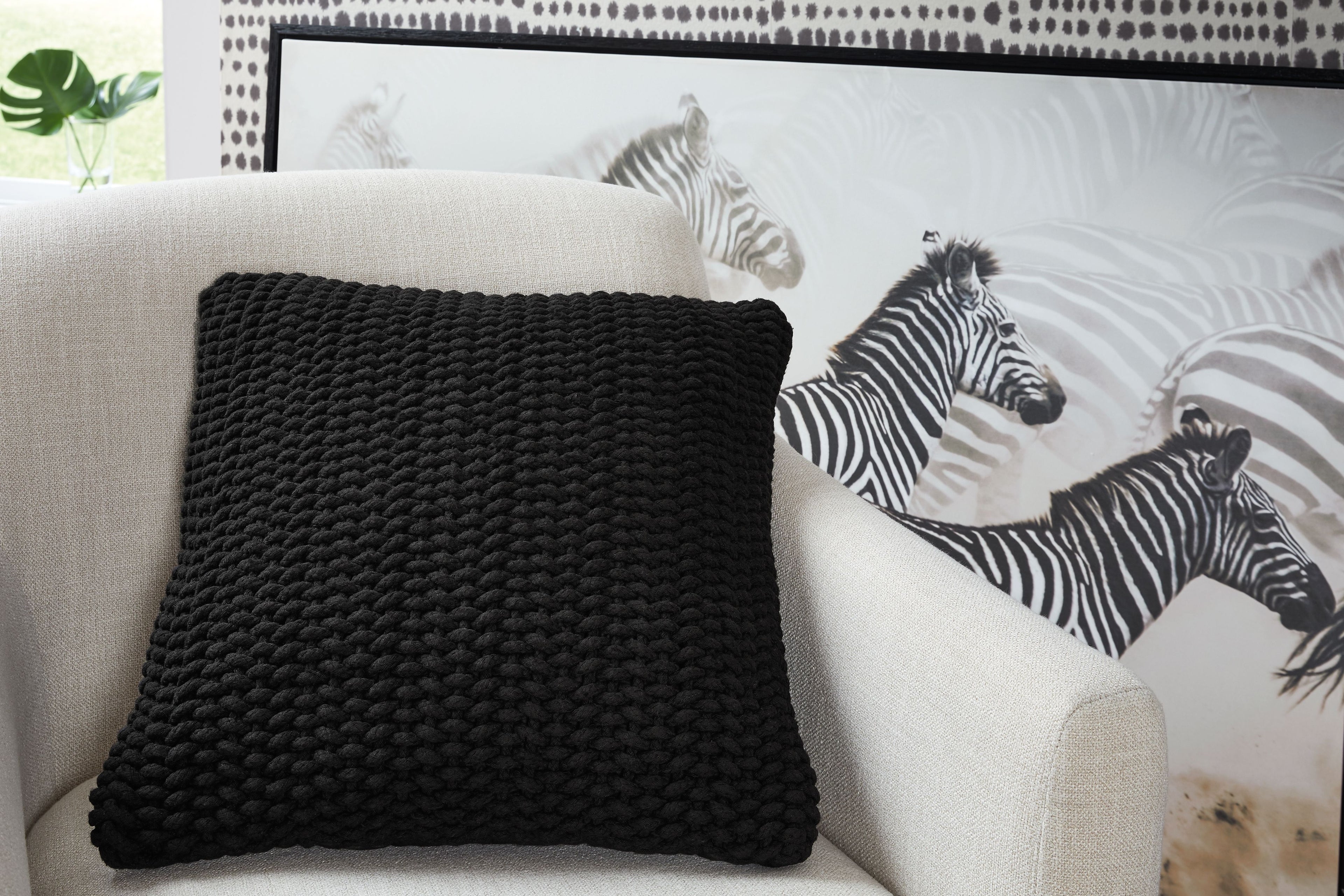 Black knitted square pillow with dense loop texture on a light upholstered surface.