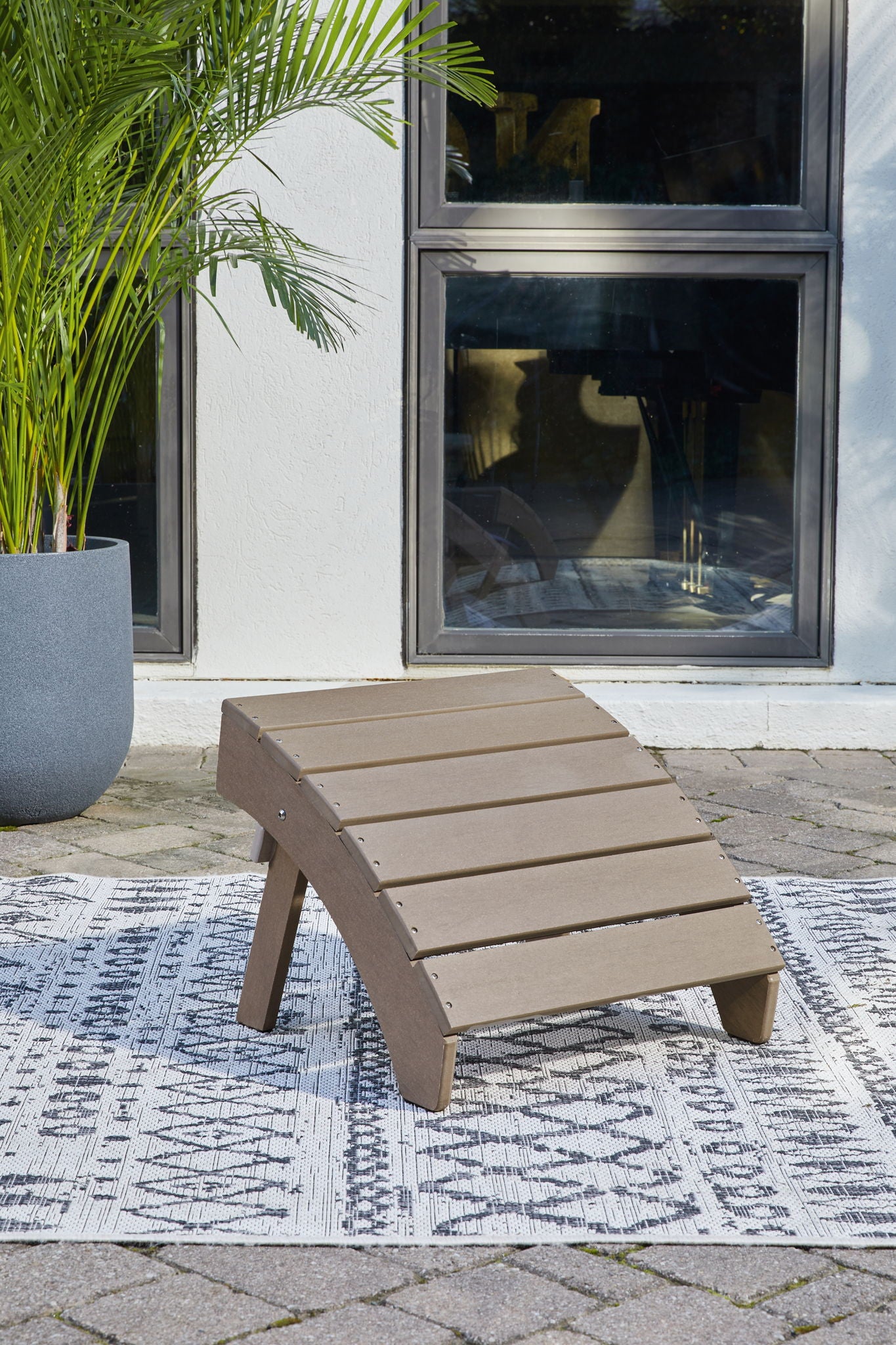 Driftwood wooden slat ottoman on ground with four legs and taupe seat.