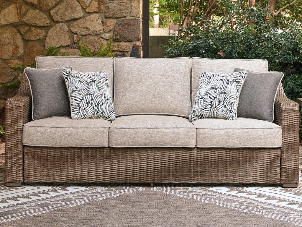 Beige sofa with woven wicker frame, two patterned back cushions on a three-cushion seat