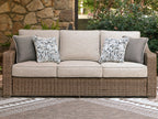 Beige sofa with woven wicker frame, two patterned back cushions on a three-cushion seat