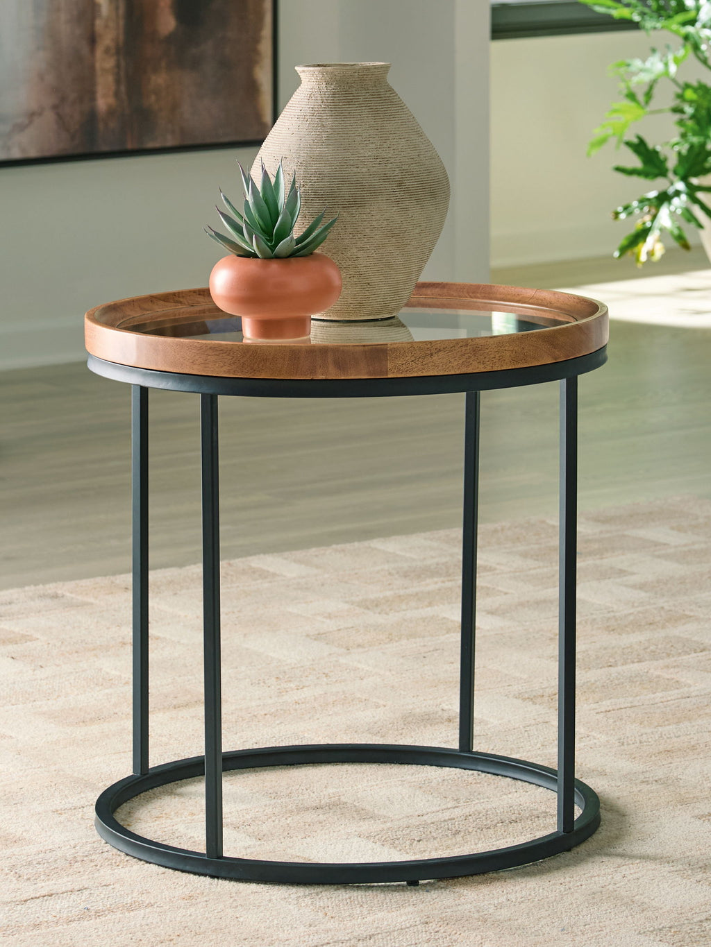 Round side table with clear glass top and light brown wood rim, black metal frame, lower shelf