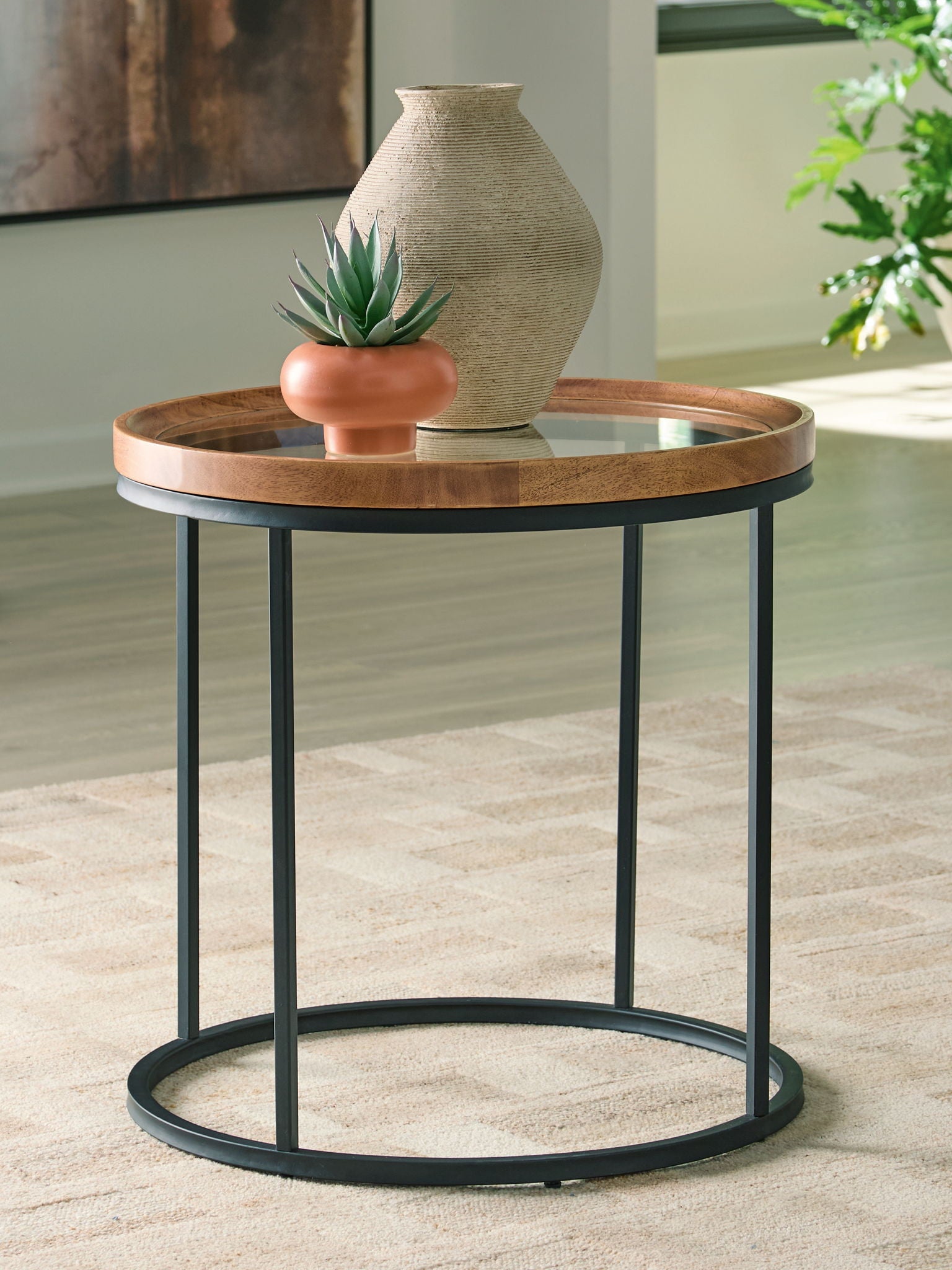 Round side table with clear glass top and light brown wood rim, black metal frame, lower shelf