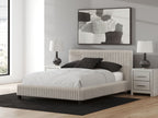 Upholstered bed with light fabric frame, white mattress and dark accent pillows