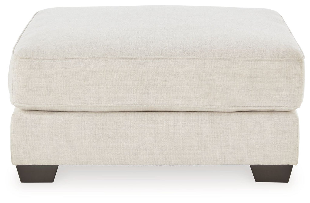 Oversized ottoman with beige fabric upholstery and dark wooden feet.