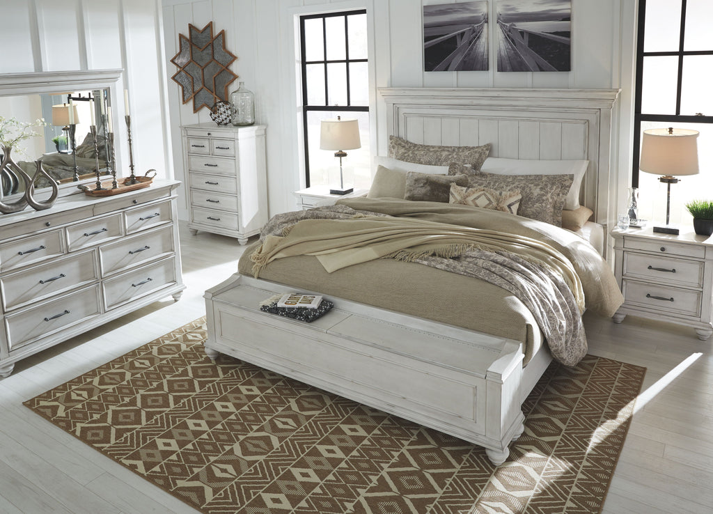 White panel bed with beige bedding and two matching nightstands, plus dresser detail