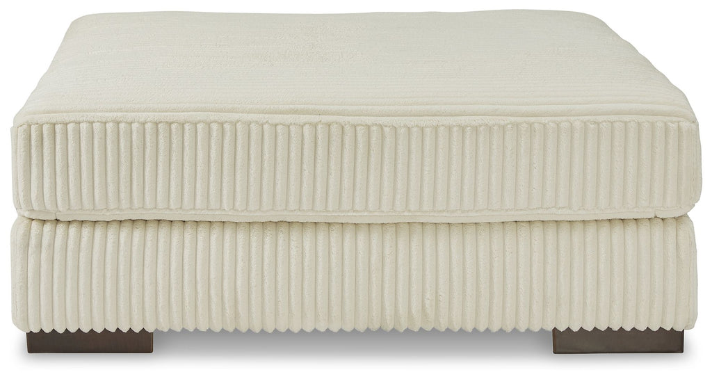 Beige upholstered ottoman with ribbed fabric and flat padded top with squared edges